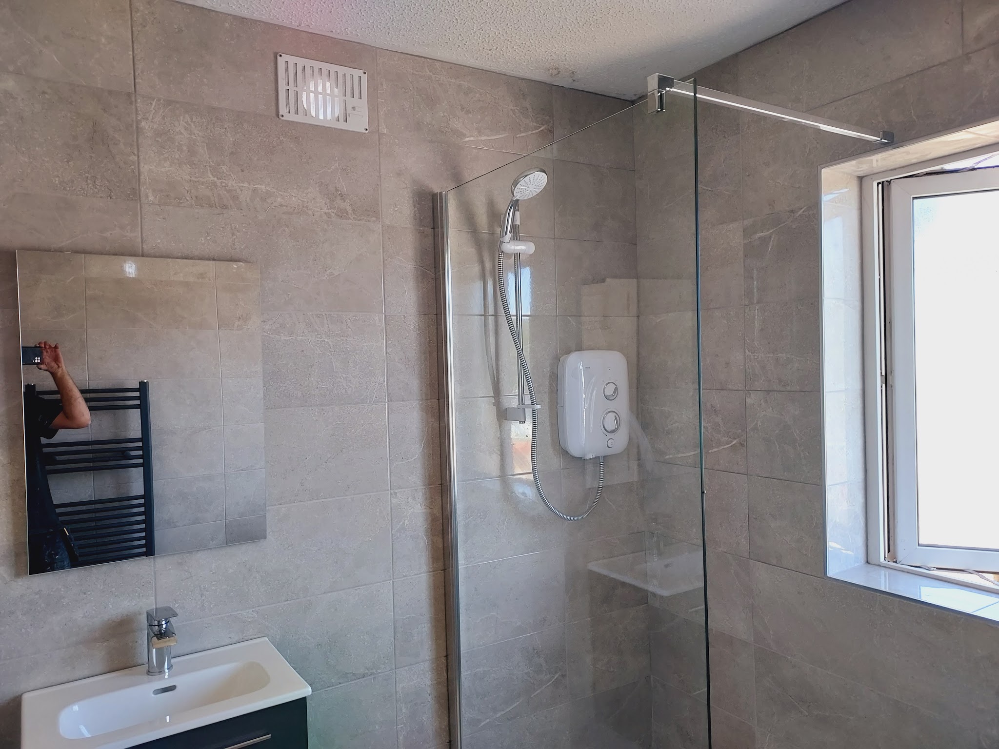 Walk-in shower beside a window with an electric shower and glass screen