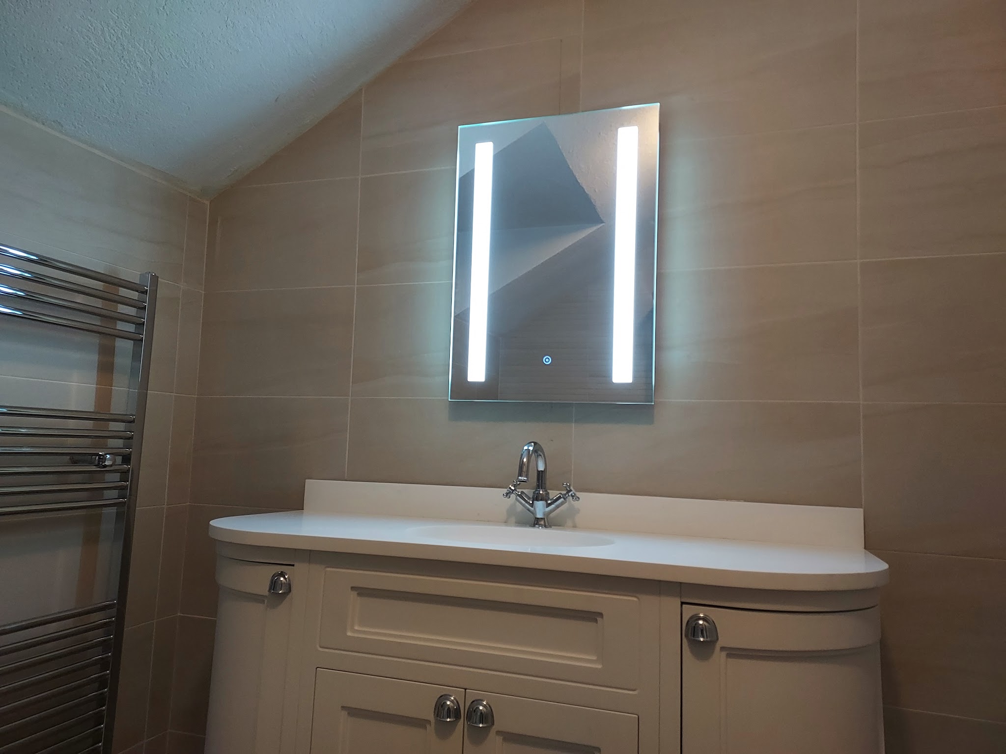Cream vanity unit with an LED mirror and a chrome towel rail under a sloped ceiling